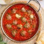 Overhead square image of meatballs in sauce with some of the cheese oozing out.