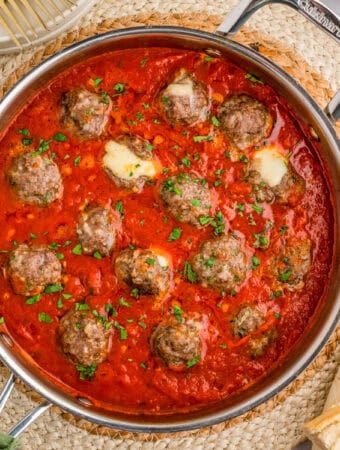 Overhead square image of meatballs in sauce with some of the cheese oozing out.