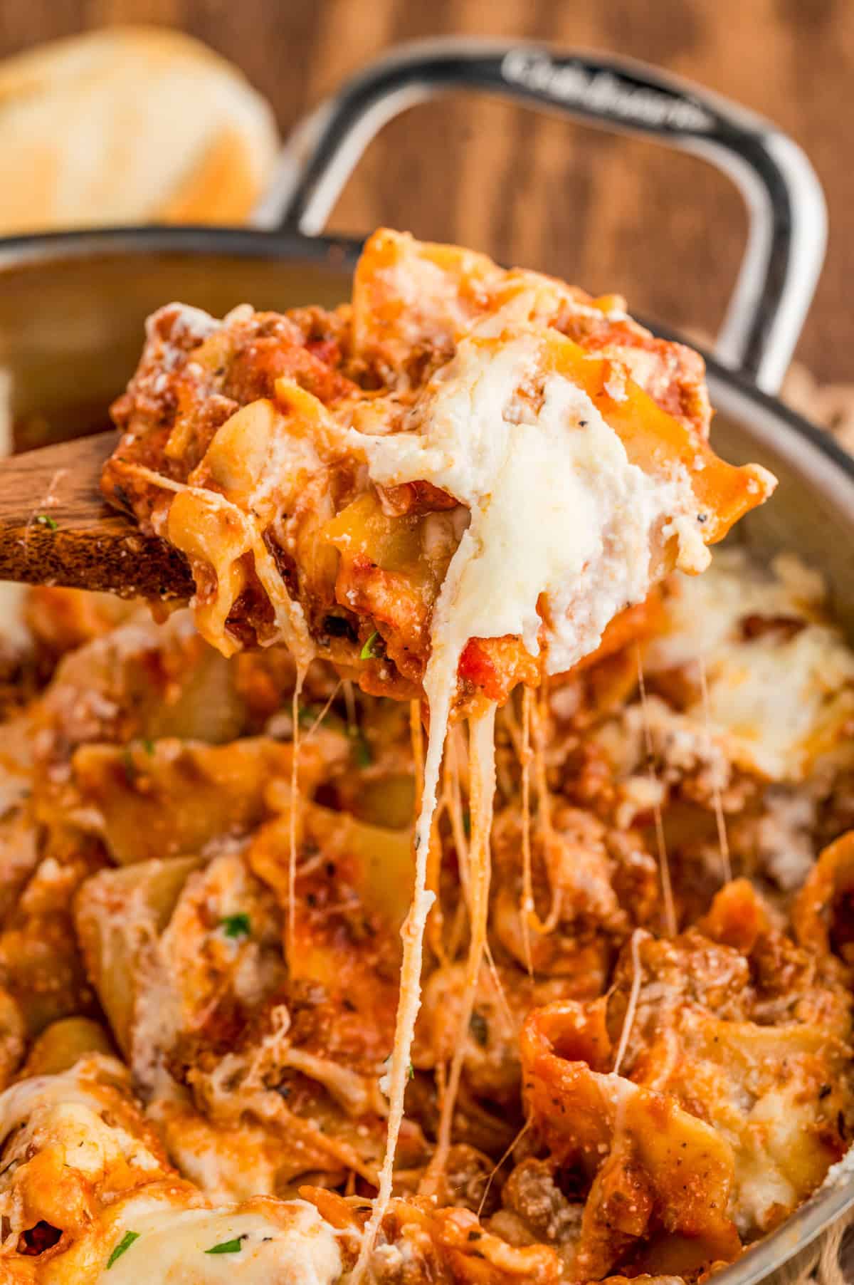 Wooden spoon scooping some of the lasagna out of the skillet showing a cheese pull.