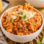 Close up of lasagna in white bowl topped with cheese and basil.