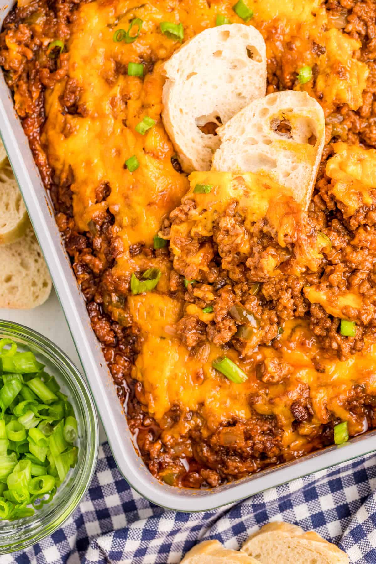 Sloppy Joe Dip overhead in baking dish with two slices of bread and green onions in bowl.