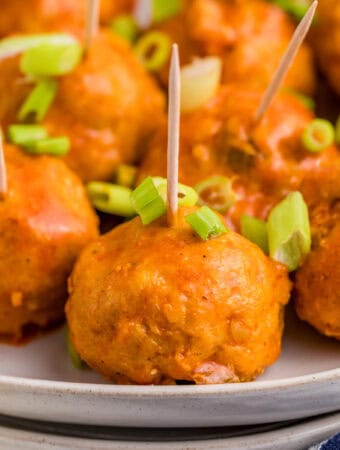 Close up square image of finished meatballs on white plate with toothpicks and green onions.