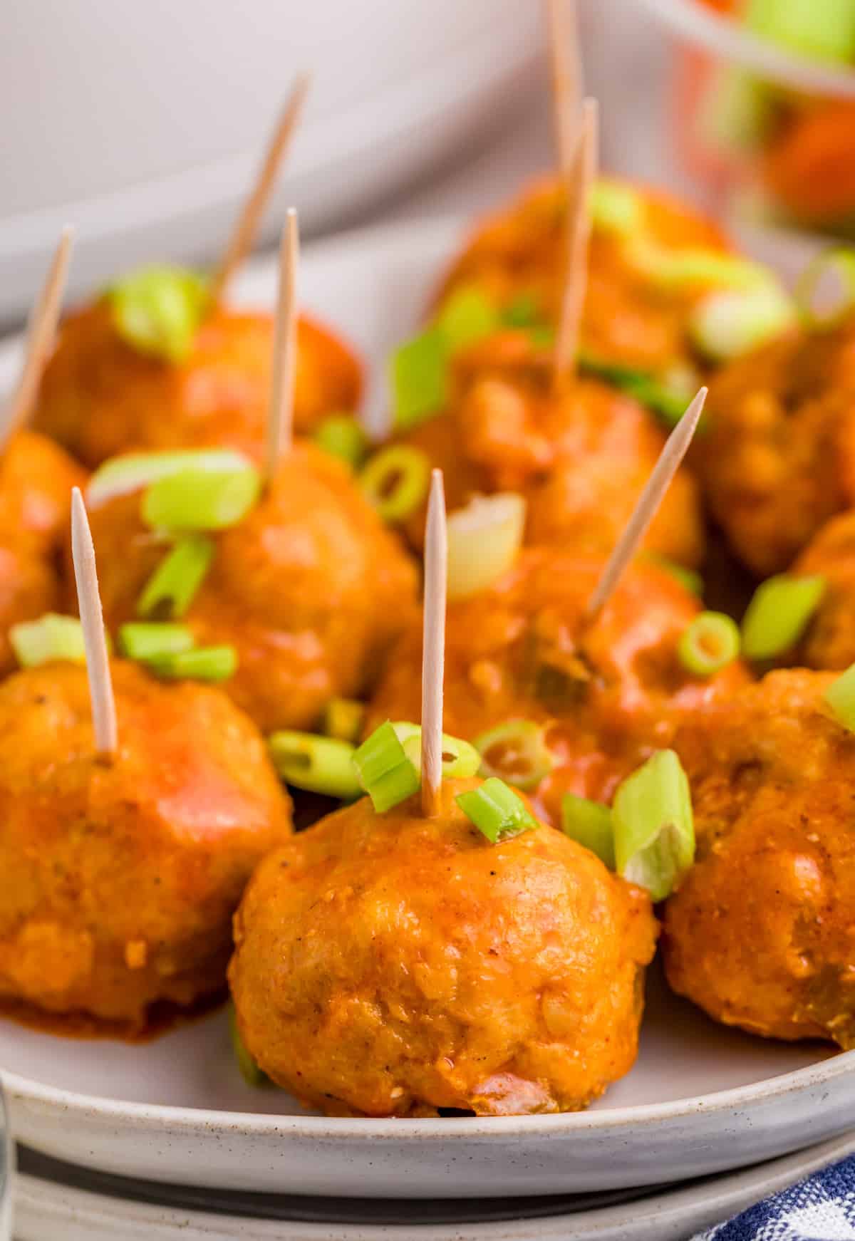 Finished Slow Cooker Buffalo Chicken Meatballs on white plate with toothpicks and green onions on top.