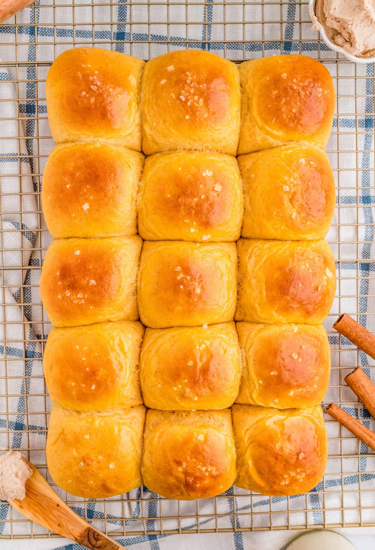 Overhead of dinner rolls on wire rack with cinnamon sticks next to rolls.