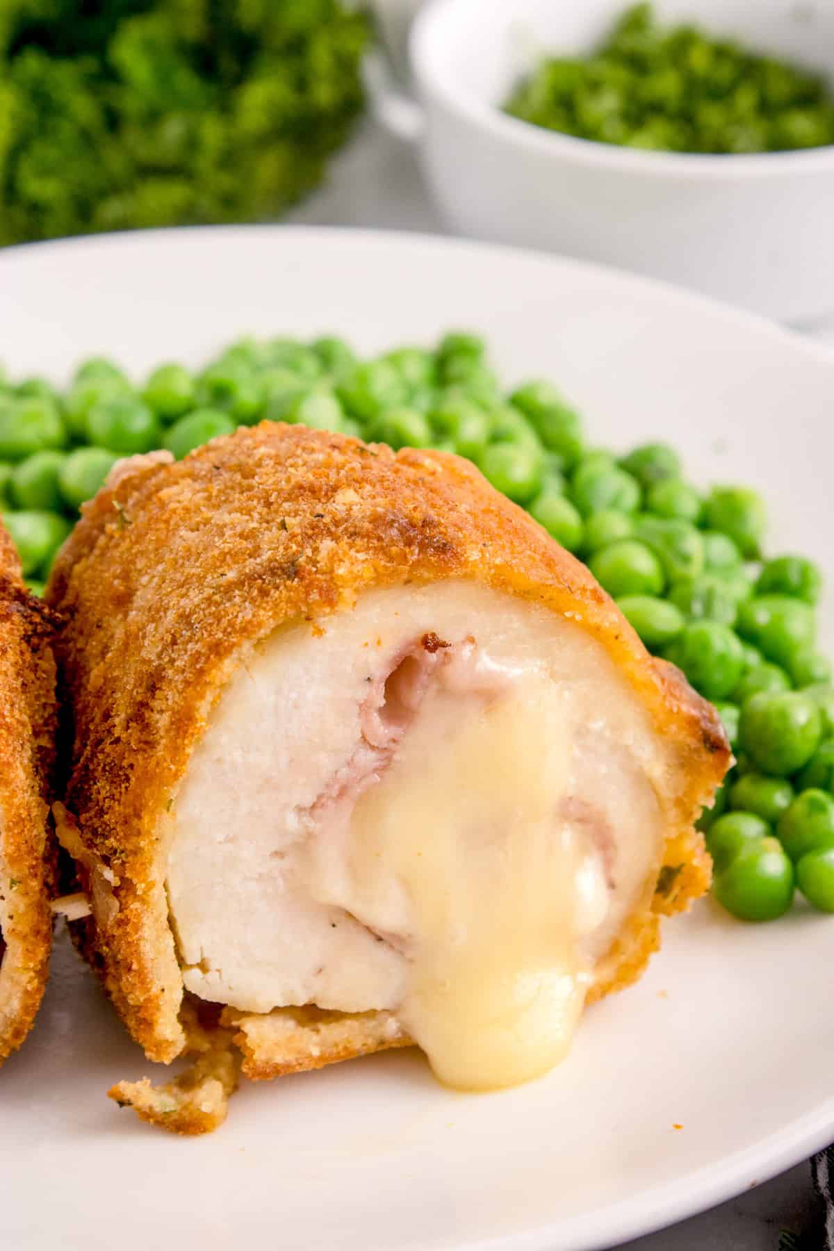 Cut Air Fryer Chicken Cordon Bleu on white plate served with peas showing cheese pouring out.