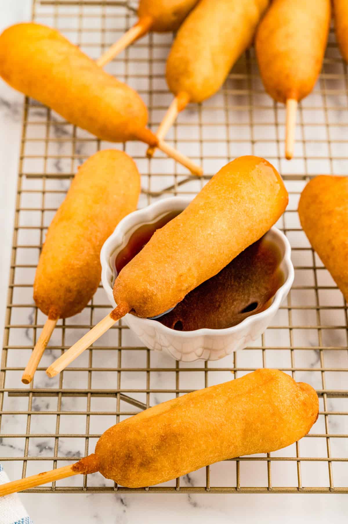 Breakfast Corndogs finished on wire rack with one over a cup of syrup.