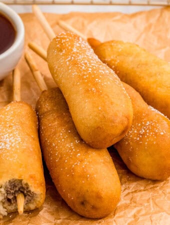 Close up of stacked corn dogs on parchment paper.