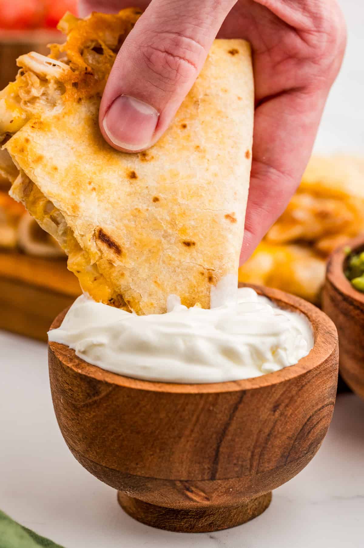 Hand dipping one triangle of a quesadilla into sour cream.