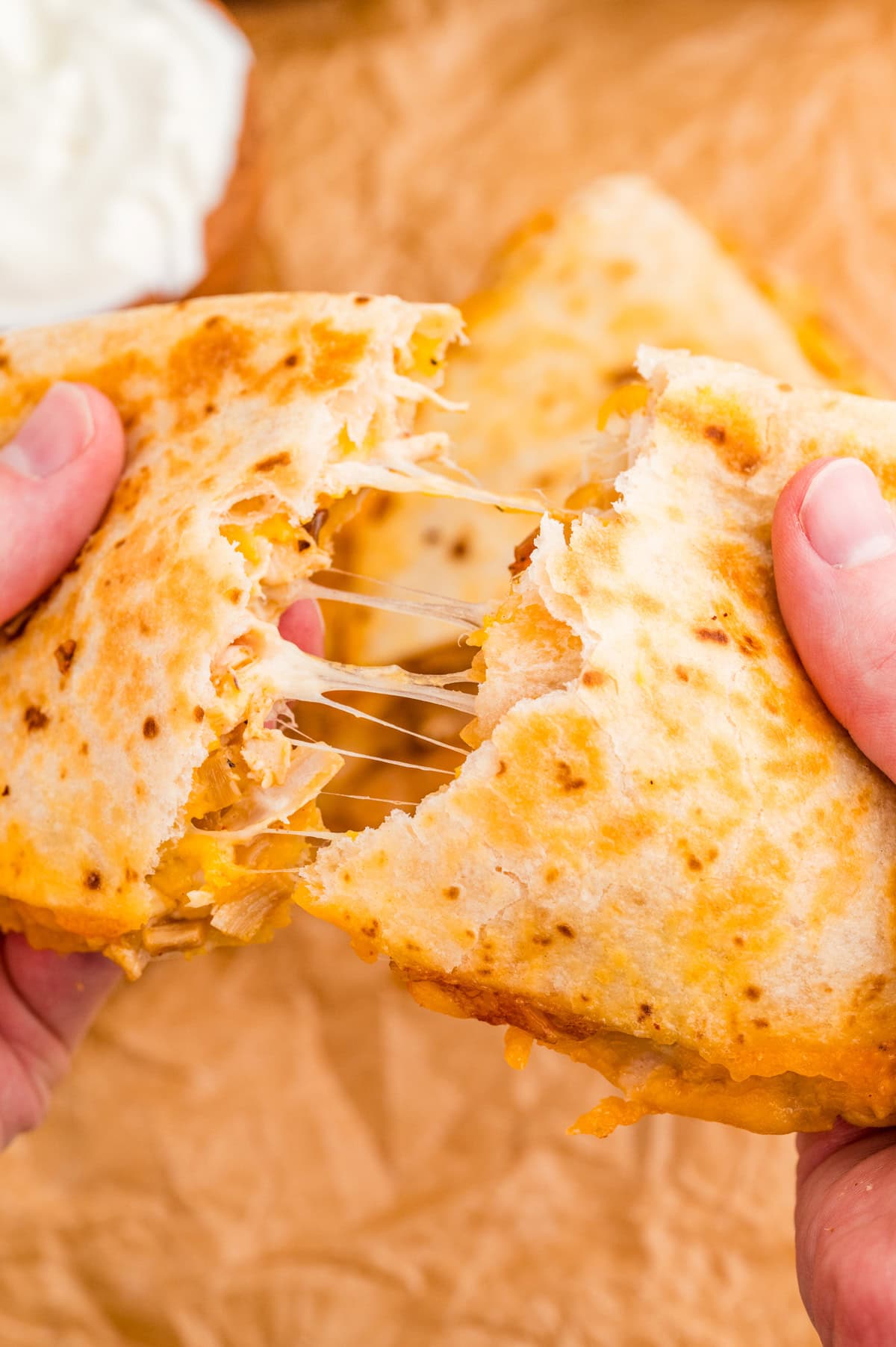 Hand pulling apart one triangle of the quesadilla showing the melted cheese.