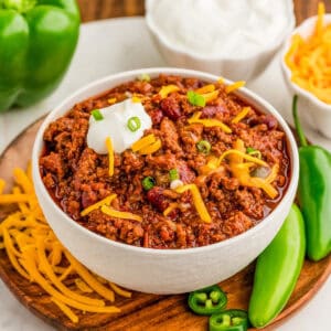 Square image of chili on bowl on wooden plate with toppings.