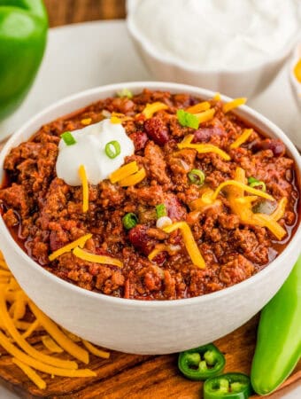 Square image of chili on bowl on wooden plate with toppings.