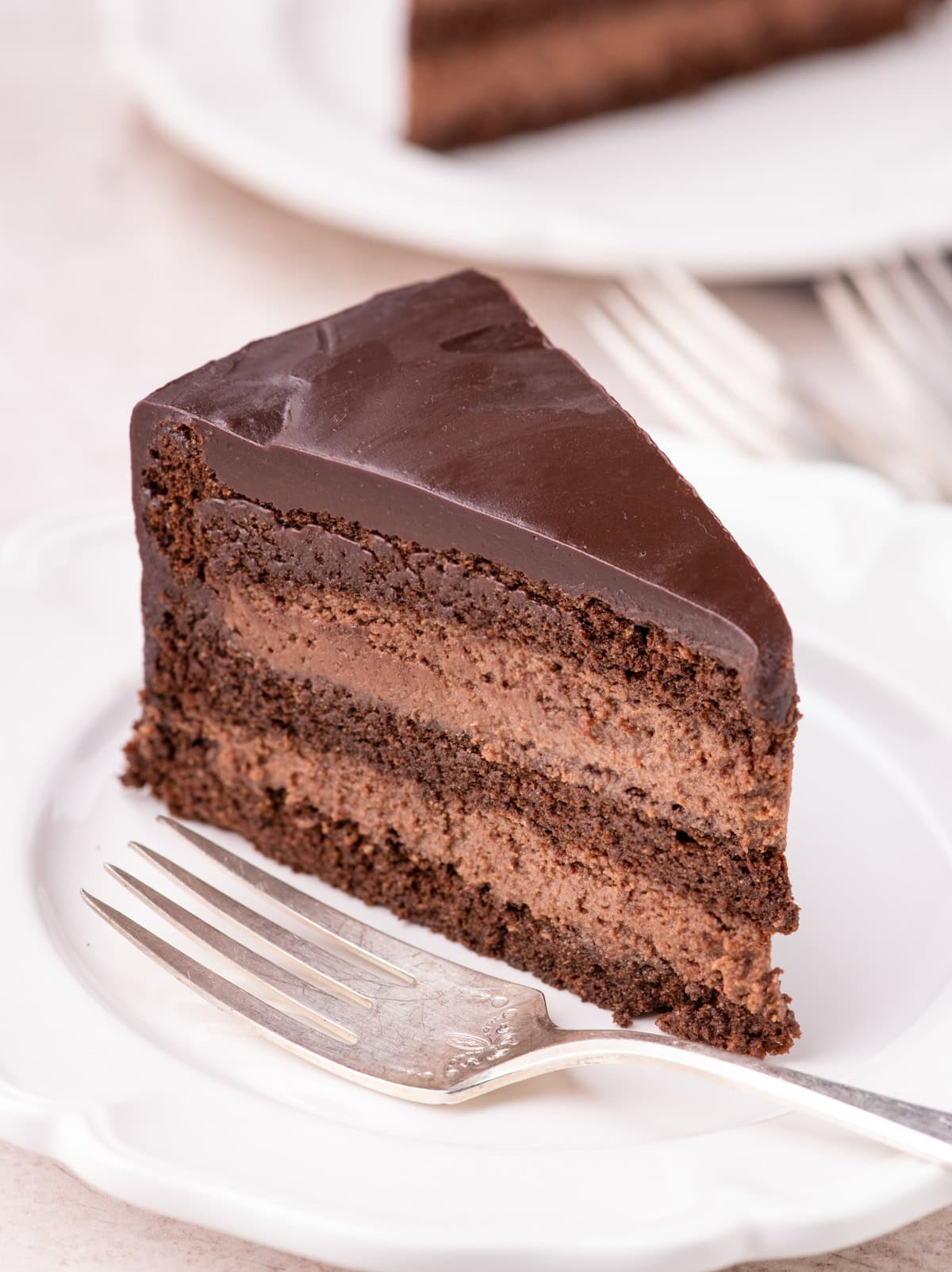 Slice of Chocolate Mousse Cake on white plate with fork showing all the layers.