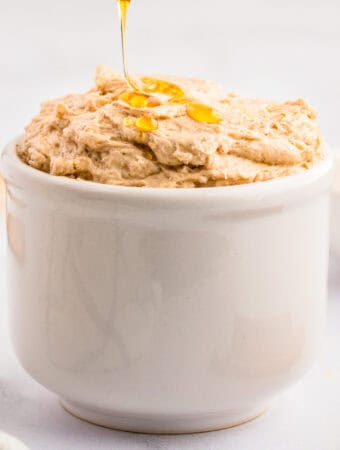 Close up square image of butter in white bowl being drizzle with honey.