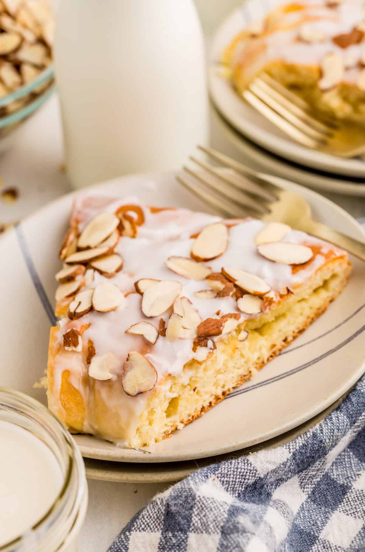 Slice of the Danish Kringle on white plate showing the toppings with milk in background.