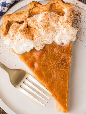 Overhead square image of a slice of pie on white plate with fork garnished.