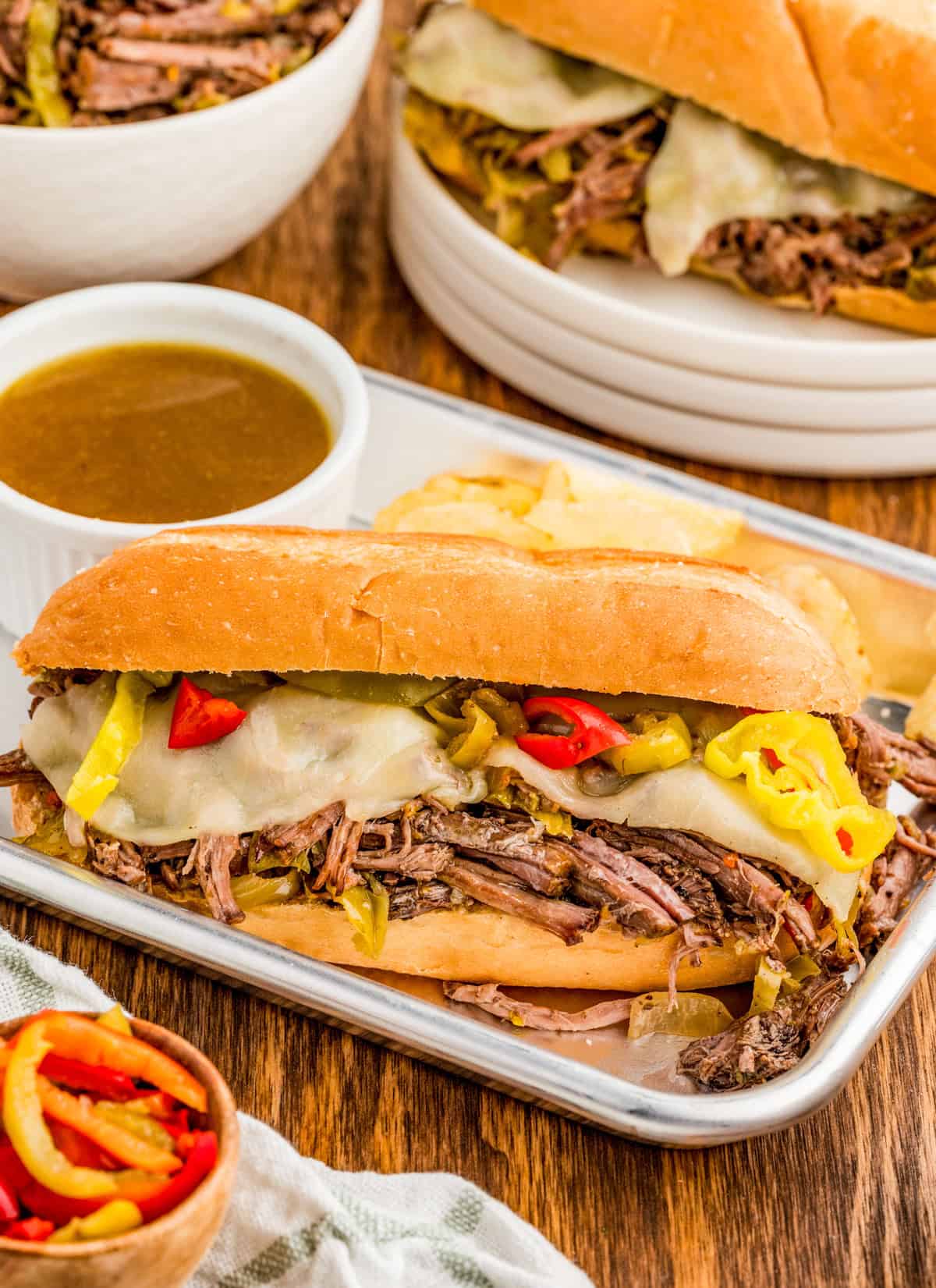 One of the Italian Beef Sandwiches on metal tray with chips and juices for dipping.