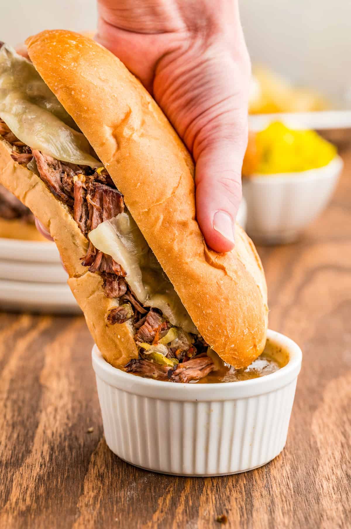 Hand dipping one of the sandwiches into the juices.