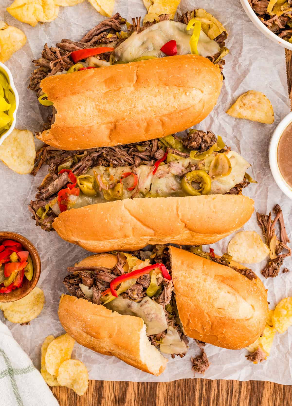 Overhead of Italian Beef Sandwiches on parchment paper showing melted cheese, peppers and beef.