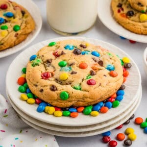 Close up square image of one cookie surrounded by mini M&M's on white plates.