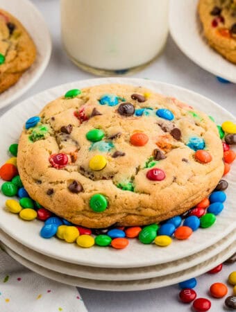 Close up square image of one cookie surrounded by mini M&M's on white plates.