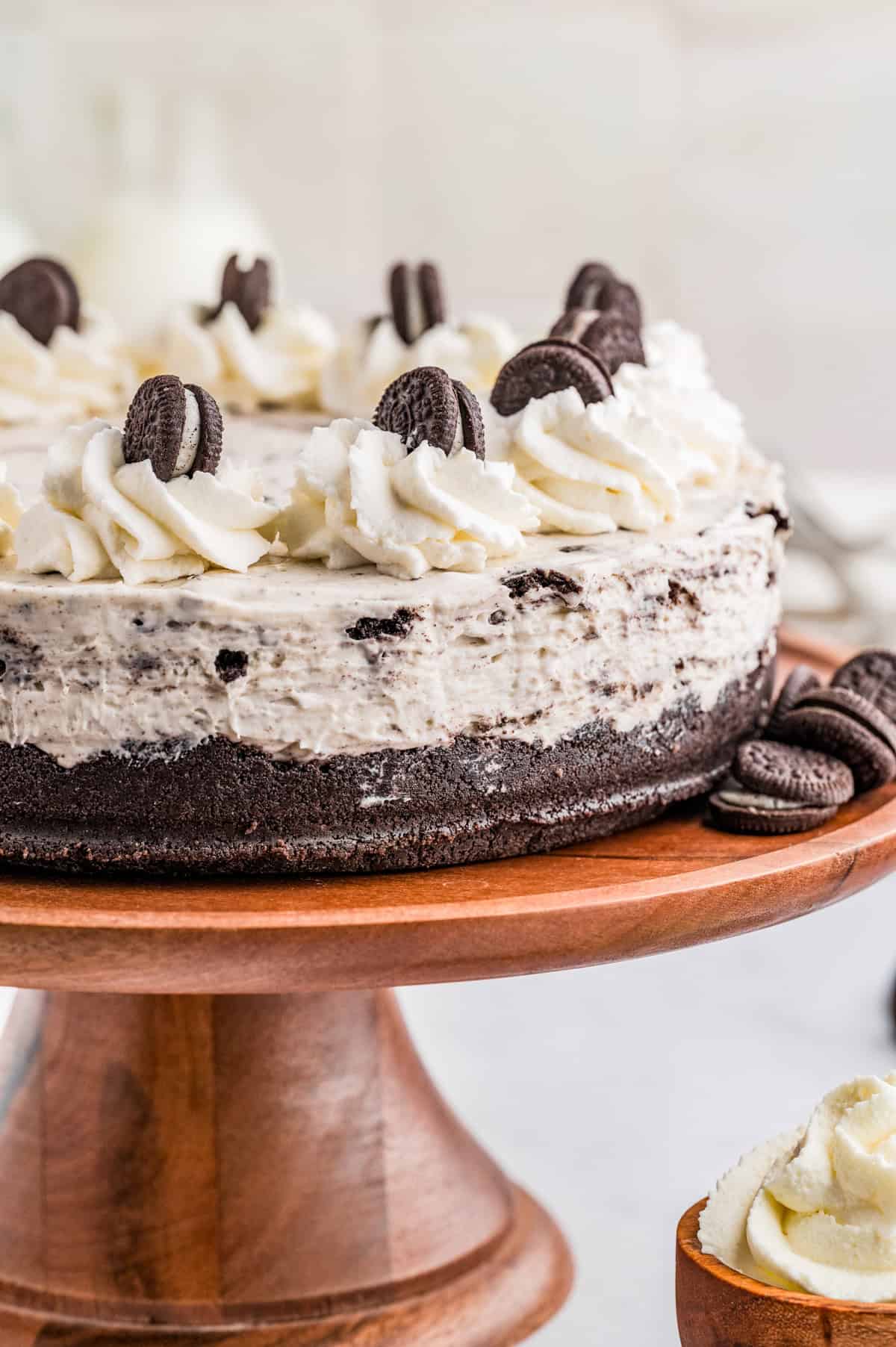 No Bake Oreo Cheesecake on wooden cake stand decorated.