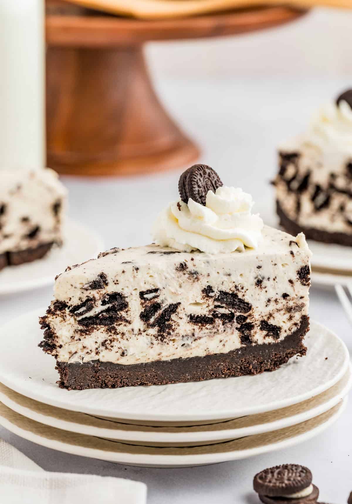 Slice of No Bake Oreo Cheesecake on white plate topped with whipped cream and a mini Oreo.