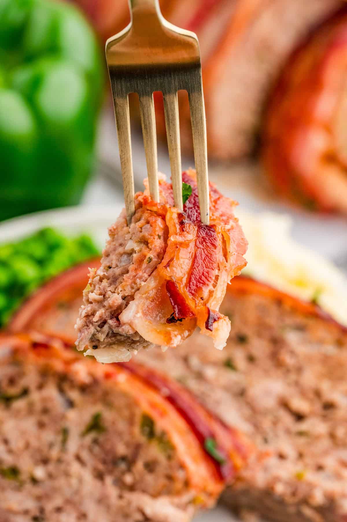 Fork holding up a bite of meatloaf from the plate.