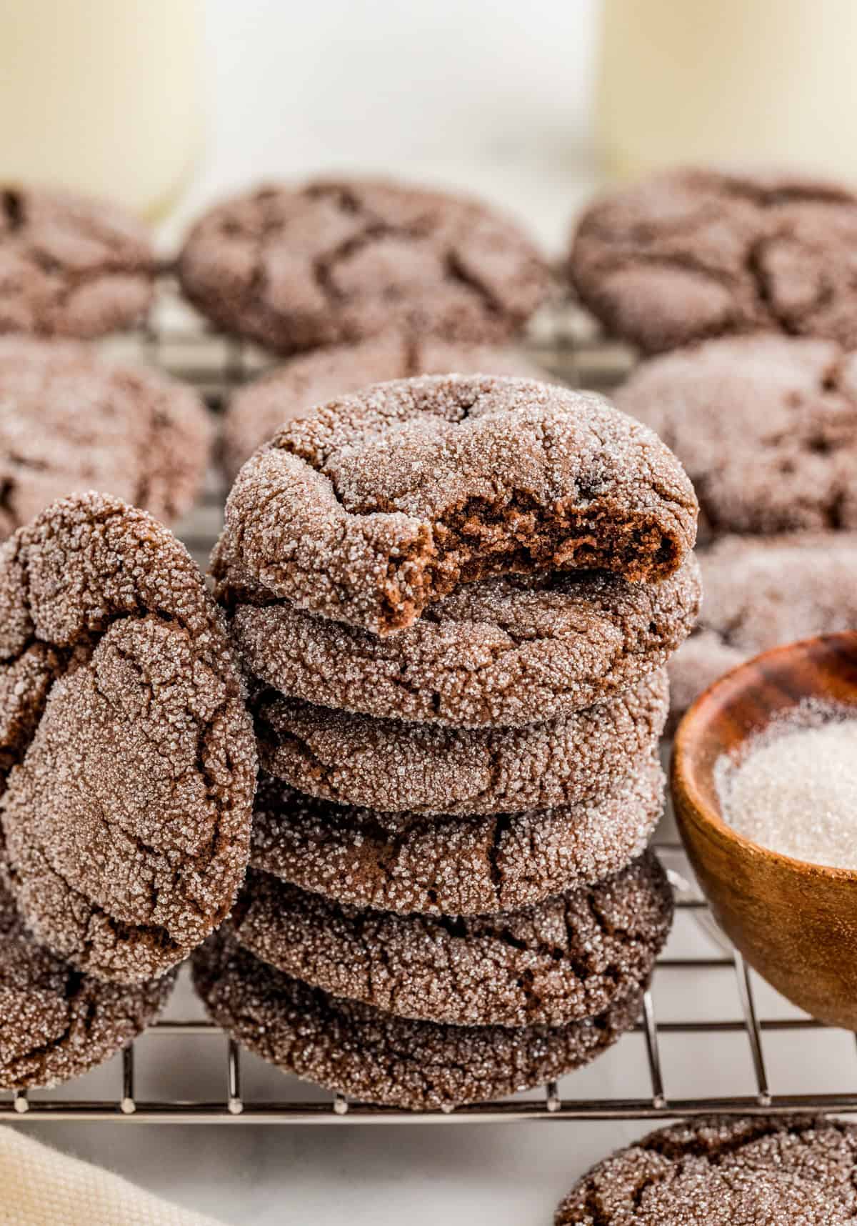 Stacked Chocolate Sugar Cookies on wire rack next to bowl of sugar with bite taken out of the top cookie.