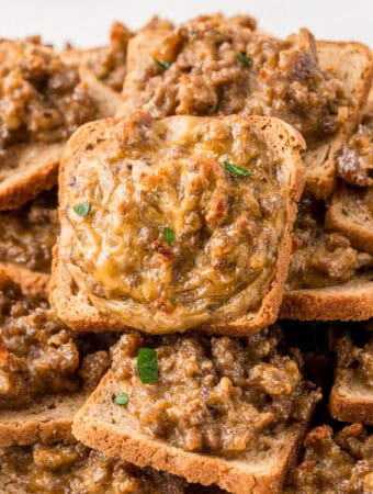 Close up square image of appetizer stacked on plate showing the meat and cheese on top of the toasted bread.