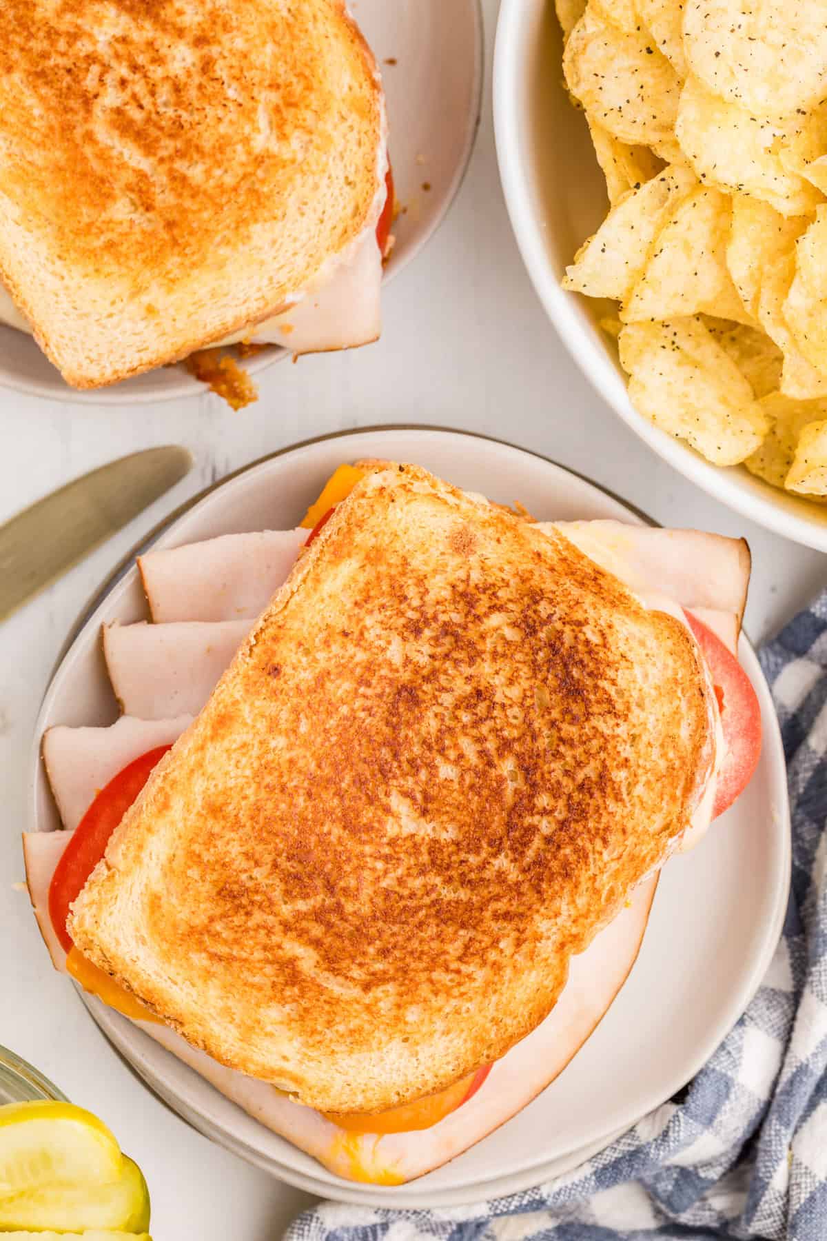 Overhead photo of finished sandwich on plate with a bowl of potato chips next to it.