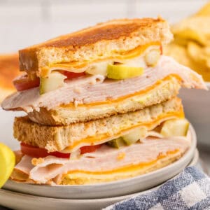 Close up square image of sandwich cut in half stacked on top of one another on plate.