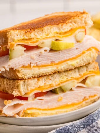 Close up square image of sandwich cut in half stacked on top of one another on plate.