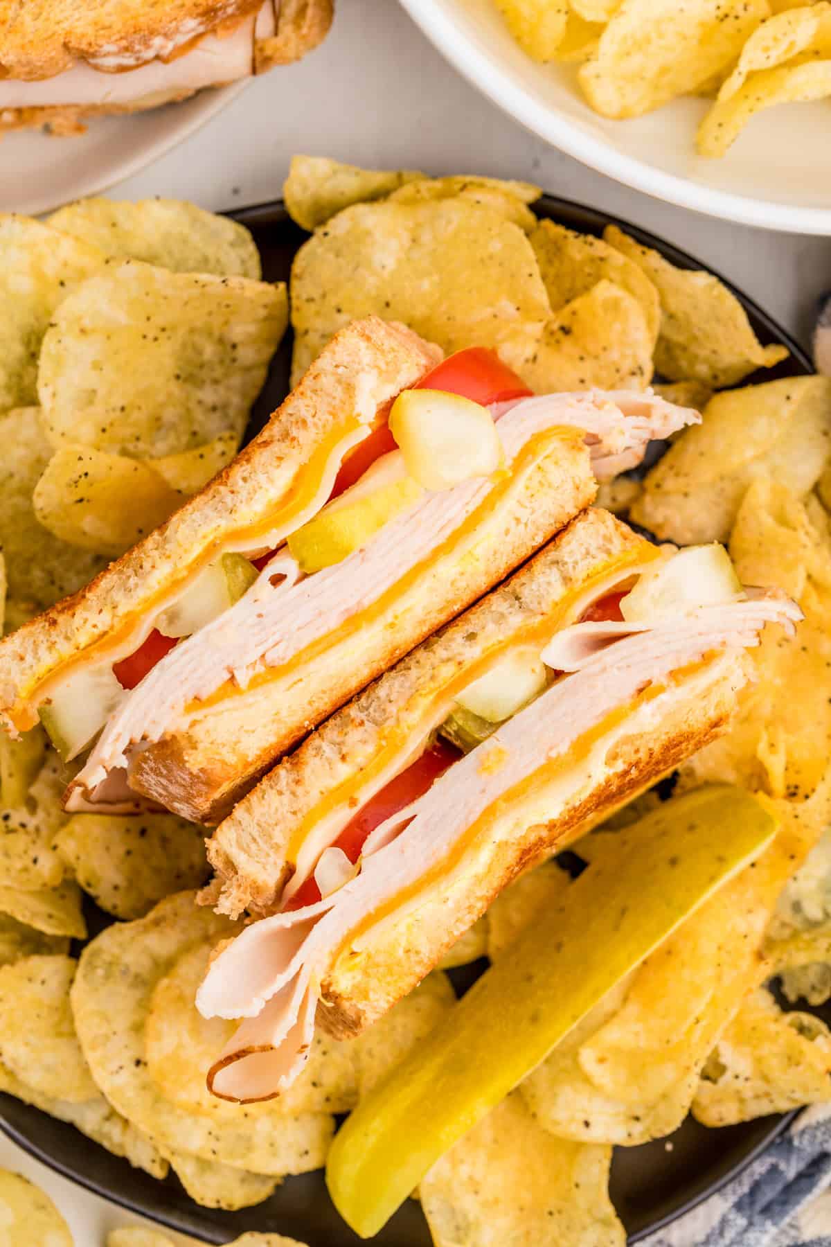 Overhead of Turkey Melt cut in half facing up on plate surrounded by potato chips.