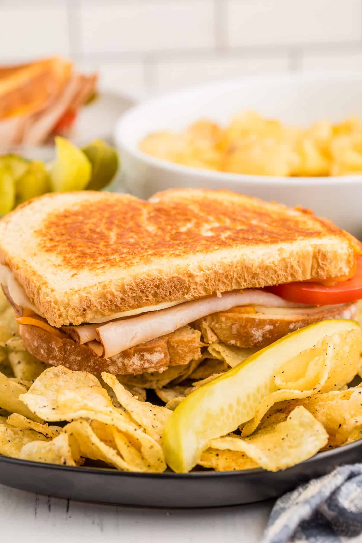 Finished sandwich on plate with potato chips and a pickle spear.