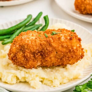 Square image of chicken topped with parsley over mashed potatoes.