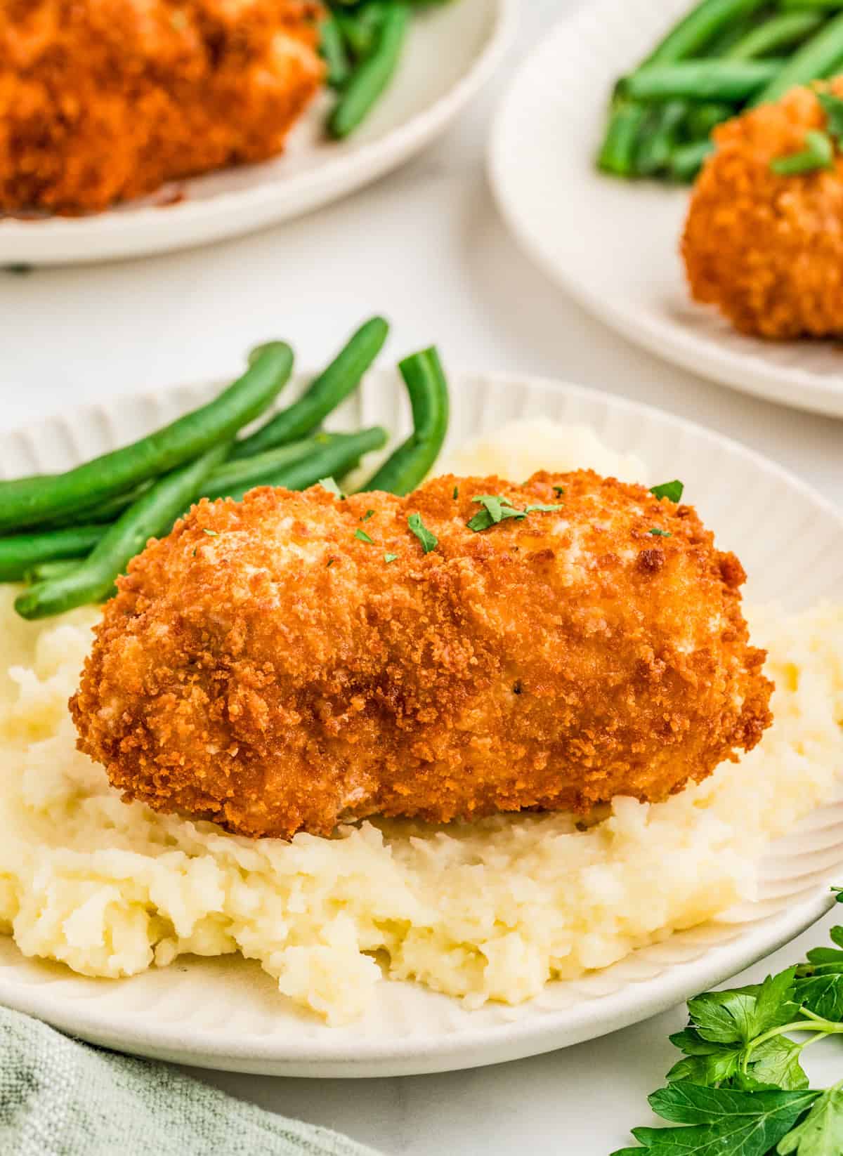 Chicken Kiev garnished with parsley over mashed potatoes with a side of green beans.