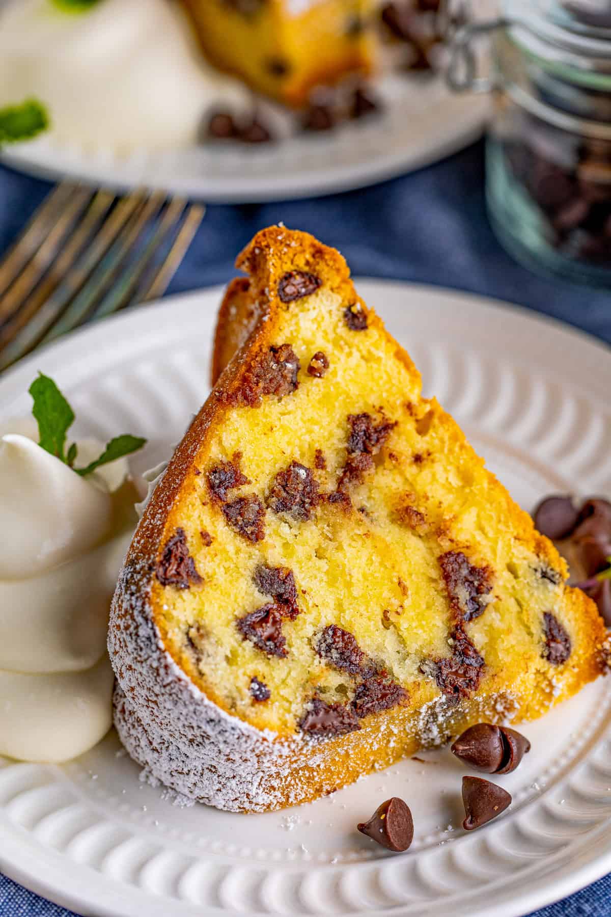 A slice of Chocolate Chip Pound Cake on white plate with whipped cream and mint.