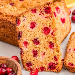 Close up square image of bread slice leaning up against loaf showing cranberries.