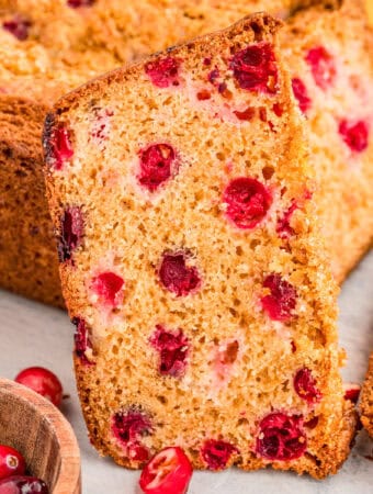 Close up square image of bread slice leaning up against loaf showing cranberries.