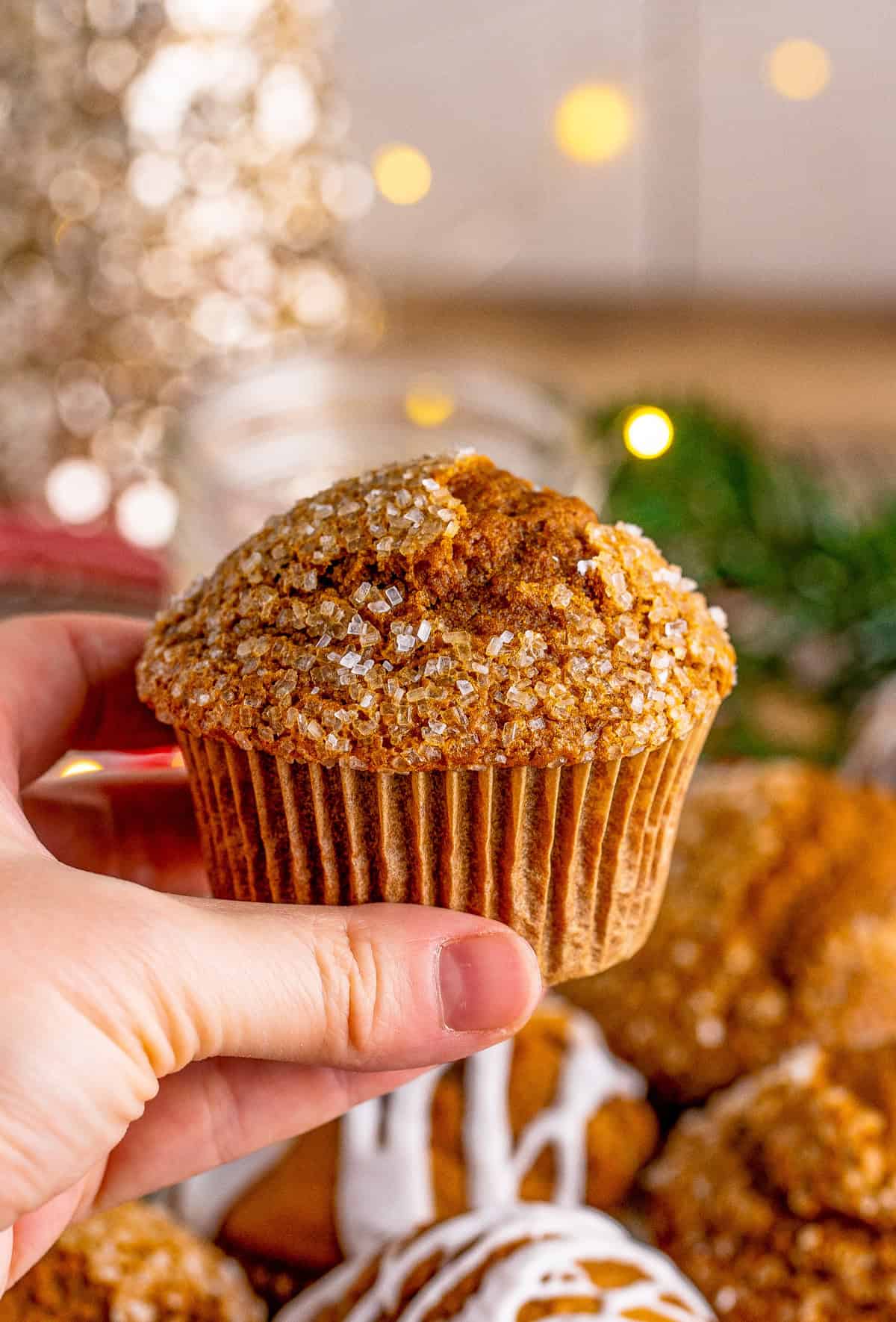 Hand holding up one of the muffins that is topped with decorators sugar.