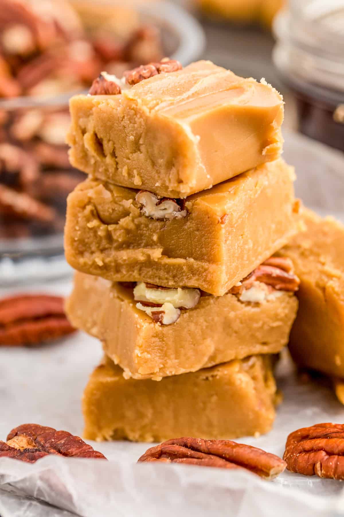 Stacked pieces of the Maple Fudge Recipe on parchment paper with pecans around it.