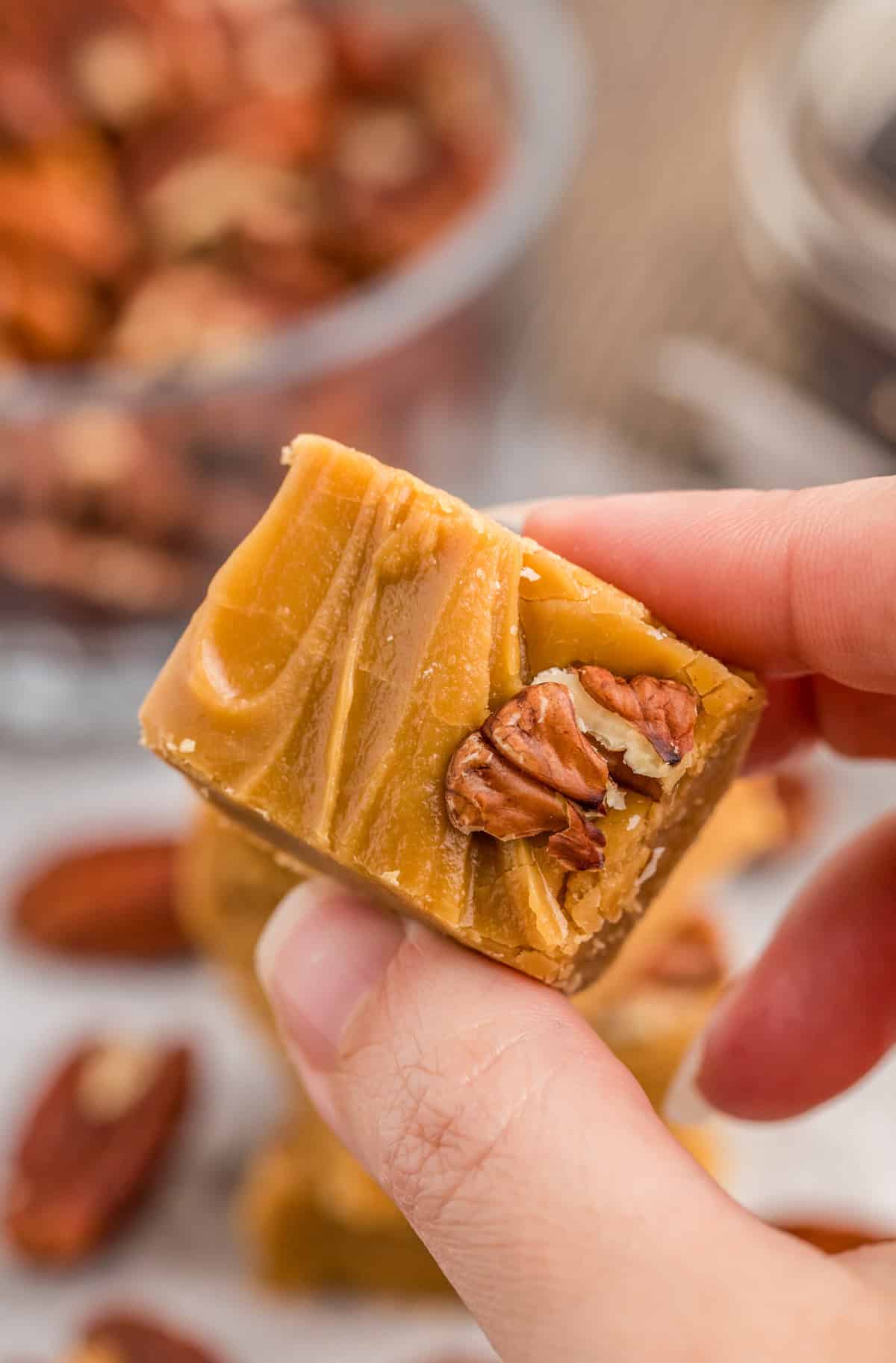 Hand holding one piece of fudge showing the nut topping.