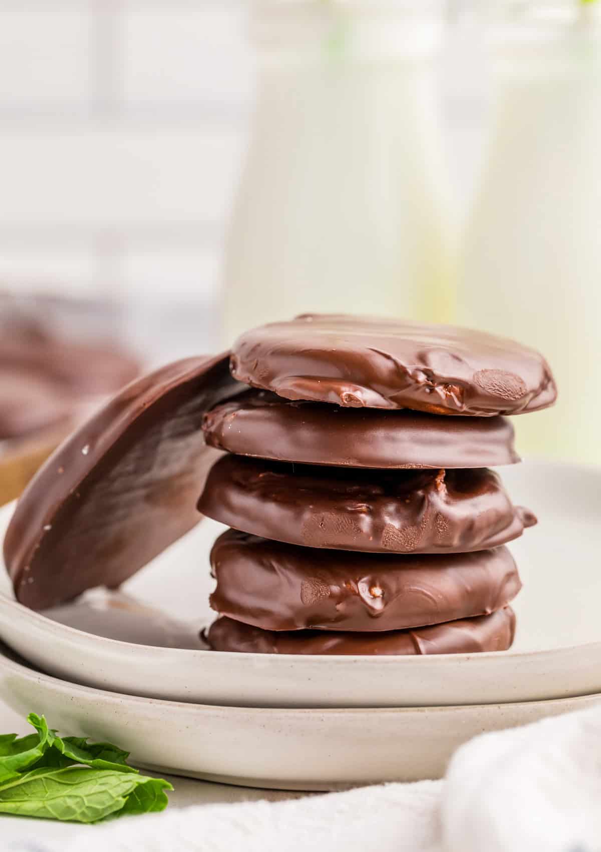 Stacked Homemade Peppermint Patties on white plate with one patty leaning against the stack.