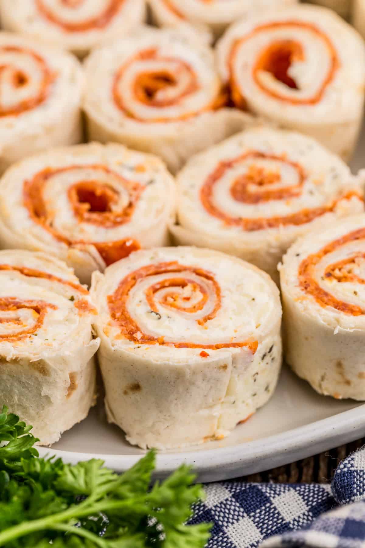 Pepperoni Pinwheels on white plate with herbs in front on plate.