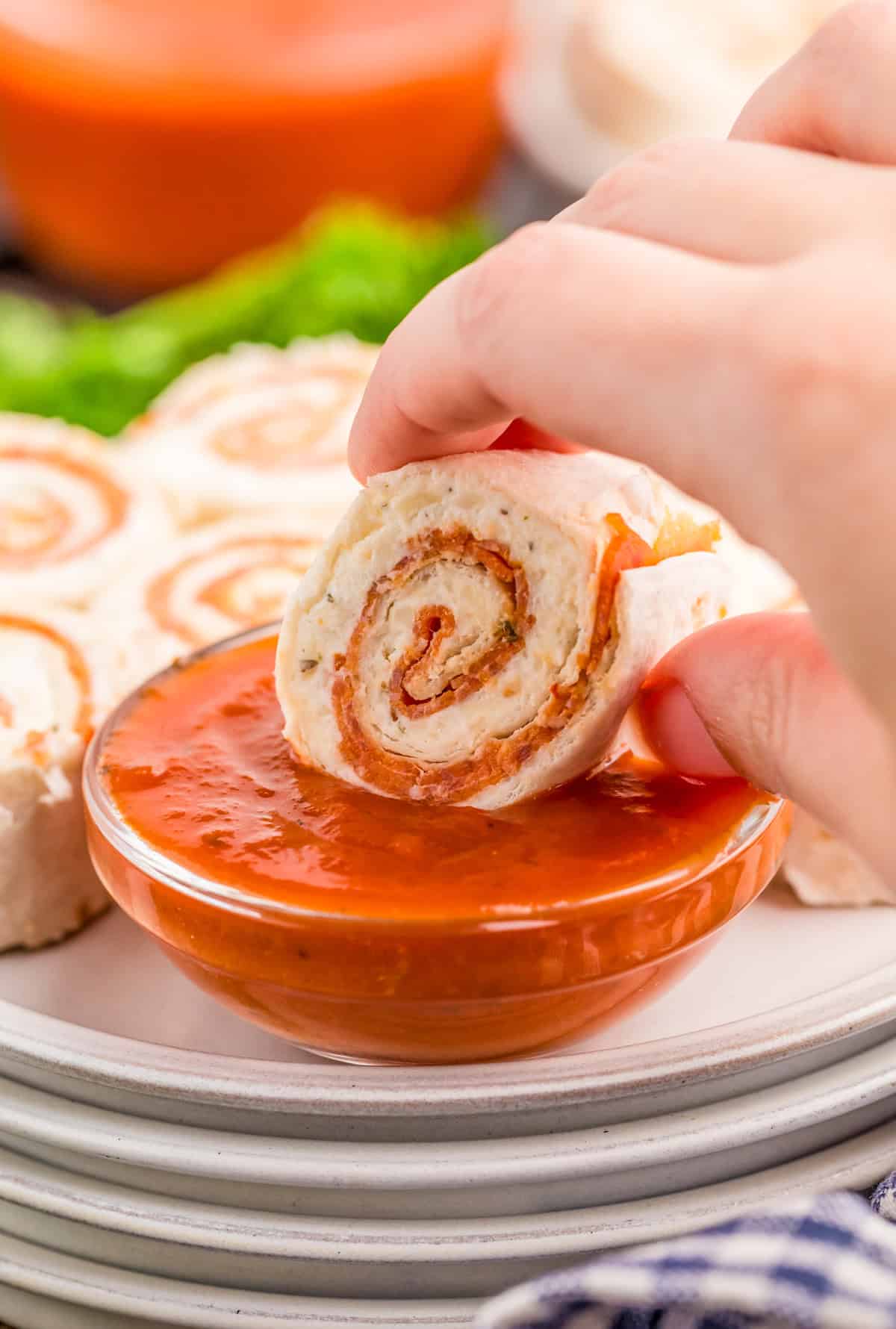 Hand dipping one of the Pepperoni Pinwheels into pizza sauce.