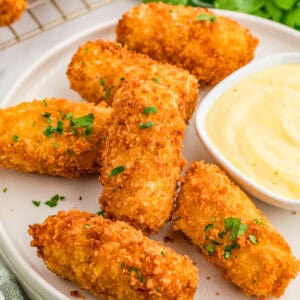 Square image of croquettes on white plate with parsley and dipping sauce.