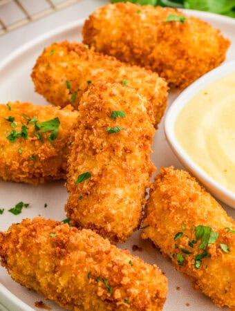 Square image of croquettes on white plate with parsley and dipping sauce.