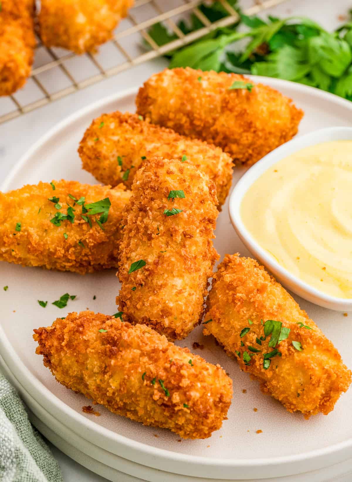 Potato Croquettes on white plate garnished with parsley with dipping sauce on plate.