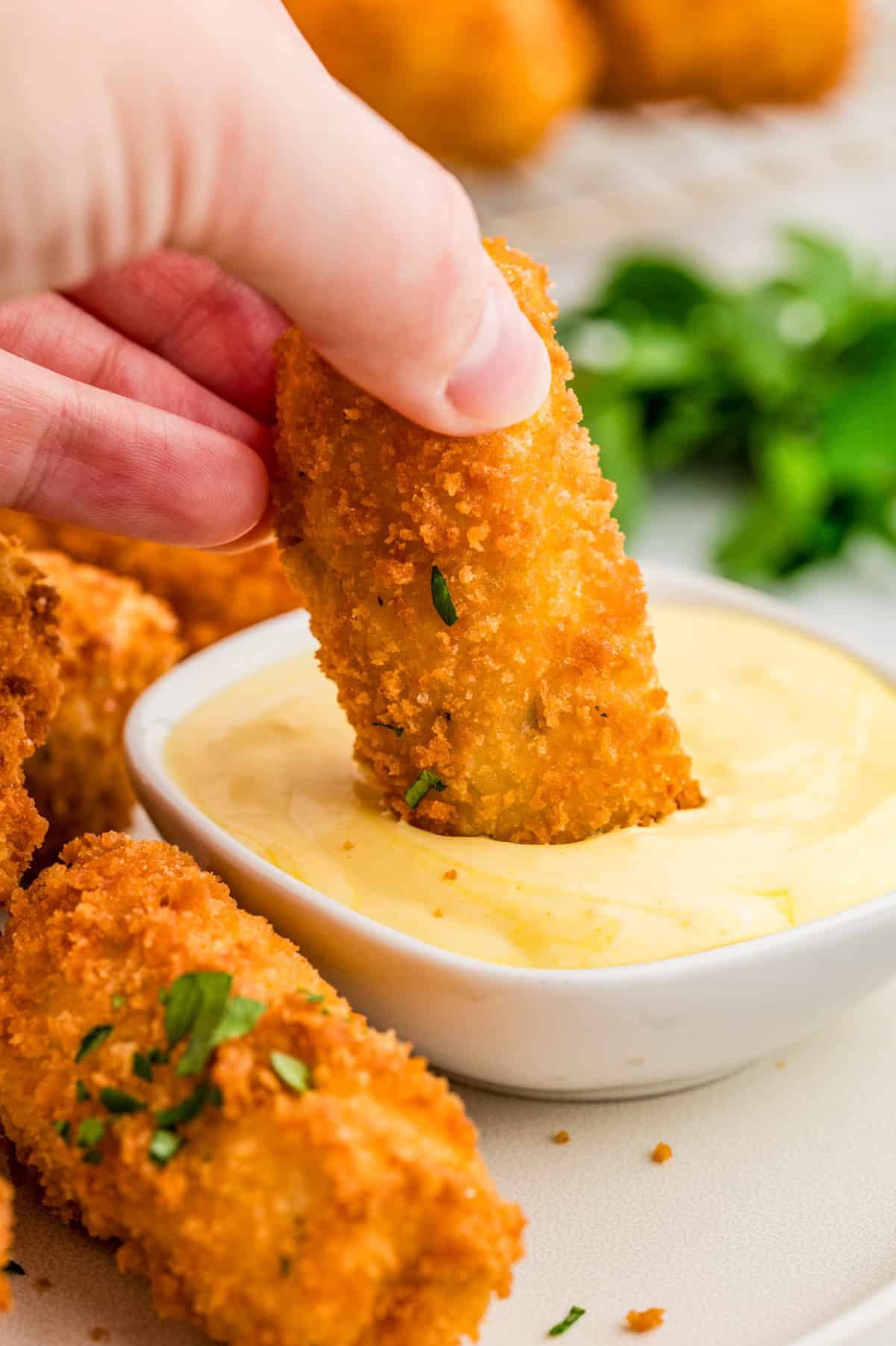 Hand dipping one of the croquettes into dipping sauce.