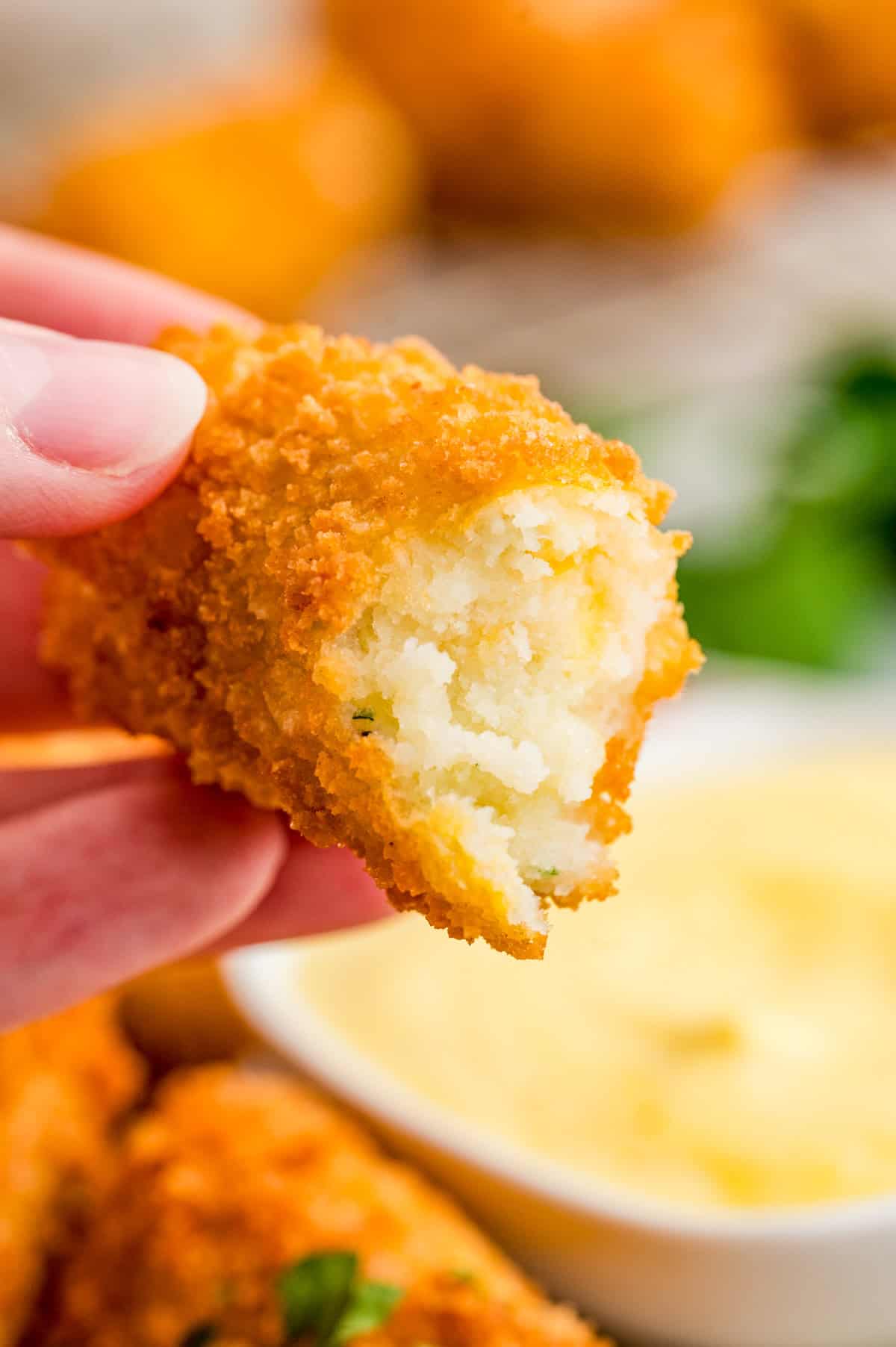 Hand holding up one of the croquettes with a bite taken out of it showing the inside.